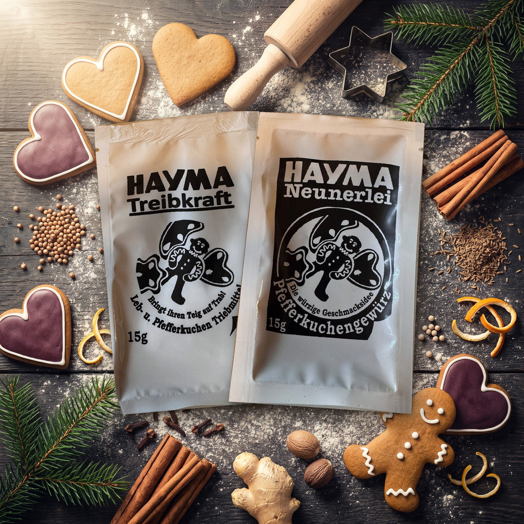 Beutel Hayma Treibkraft und Hayma Neunerlei nebeneinander auf einem Backtisch mit Lebkuchen, Zimt, Nelken, Ingwer, Muskatnuss und Tannenzweigen